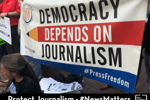 protestor holding sign that reads "Democracy Depends on Journalism"