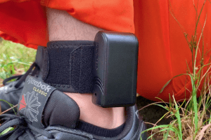 Close up of the black ankle bracelet on the man in the orange jumpsuit