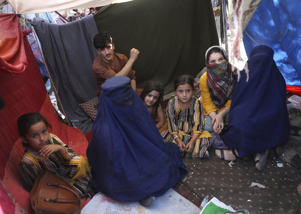 a group of Afghan women and children sit inside a tent