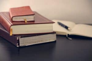 stack of books on desk with open notebook and pen