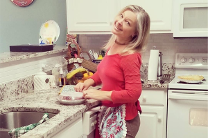 Shawna Kenney in her kitchen, smiling at the camera and simultaneously crimping a pie crust