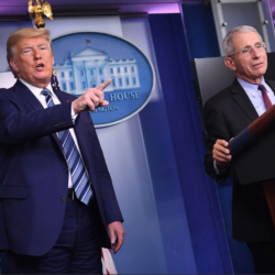 Anthony Fauci at the podium in the White House, standing next to President Trump who is pointing at the audience
