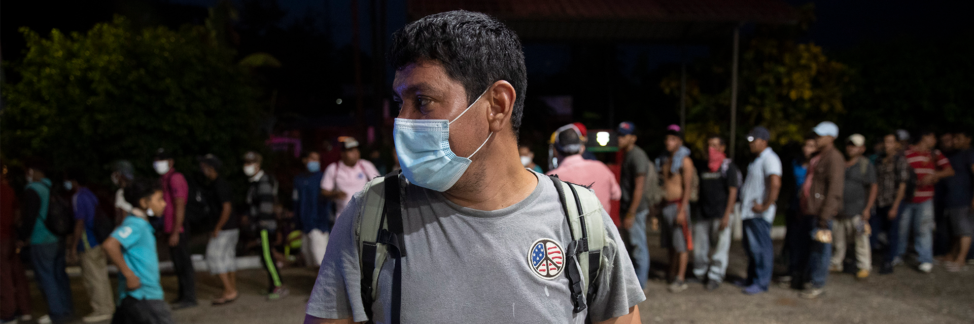 Centered and in front: a migrant at a gas station/food mart in Morales, Guatamela; more migrants in the background