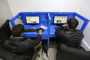 two men at an internet cafe looking at screens