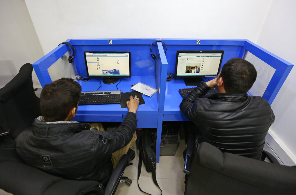 two men at an internet cafe looking at screens