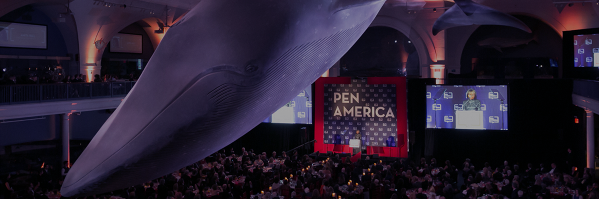 Photo from 2019 PEN America Literary Gala, with whale overhead at the American Museum of Natural History and PEN America stage/audience in the background