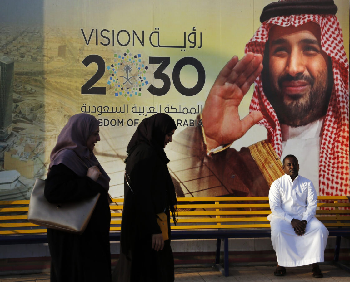 People walk past a banner showing Saudi Crown Prince Mohammed bin Salman