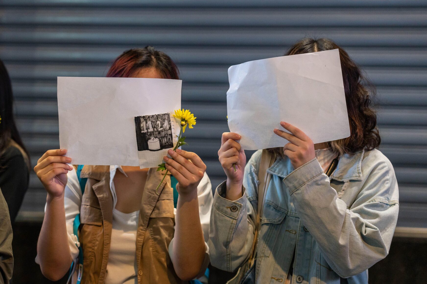 Two people hold blank pieces of paper in front of their faces.