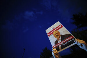 Hands hold up a sign of Jamal Khashoggi with the night sky in the background