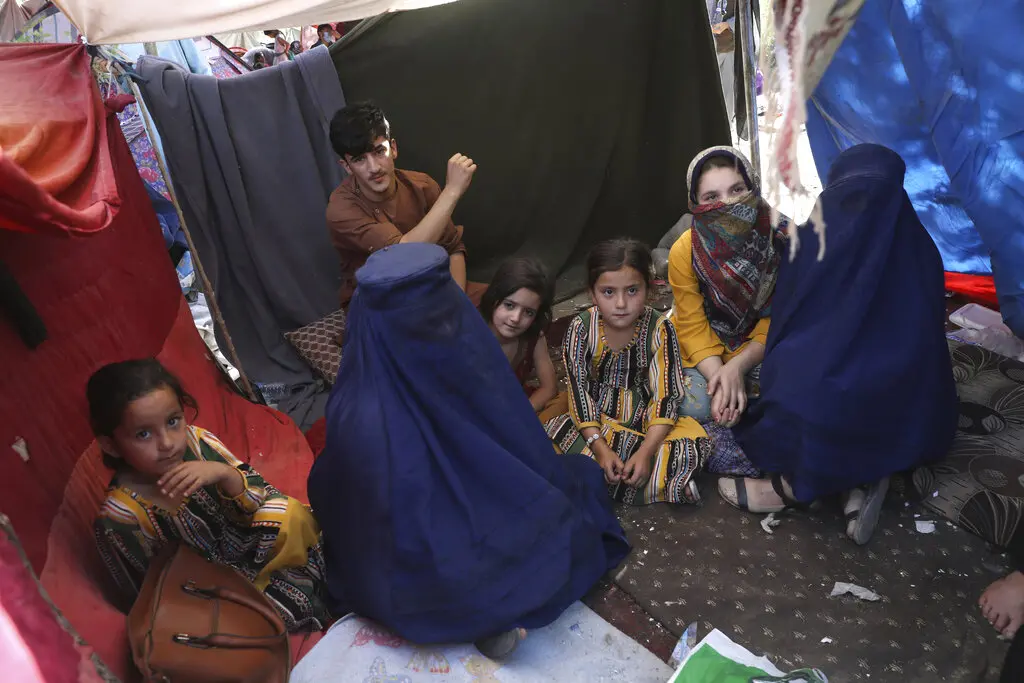 a group of Afghan women and children sit inside a tent