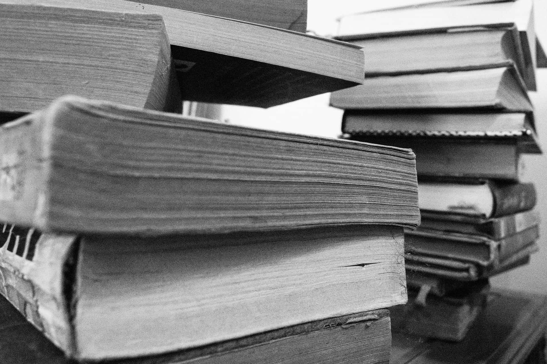 A close-up, black-and-white photo of several stacks of old, worn books arranged haphazardly, with pages and edges visible in the foreground and background.