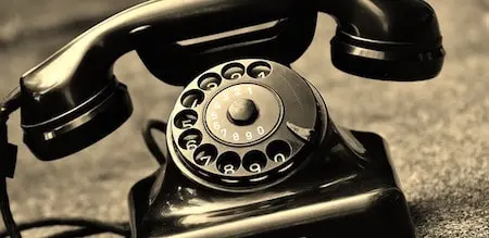 A vintage black rotary dial telephone with the receiver resting on top of the phone, placed on a textured surface.