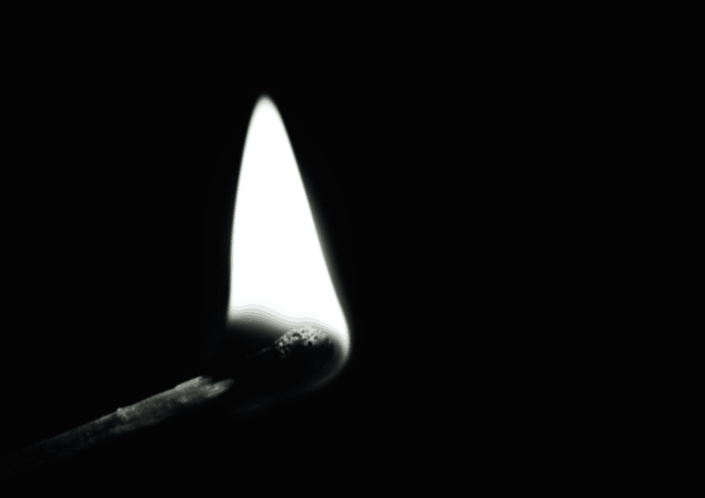 A single matchstick burning with a bright flame against a dark, black background.