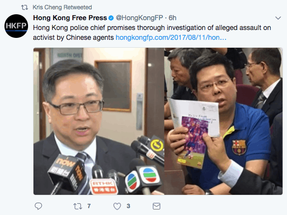 A man in a suit speaks to reporters holding microphones, while another man beside him holds up a booklet and gestures. Several people are visible in the background at what appears to be a press event.