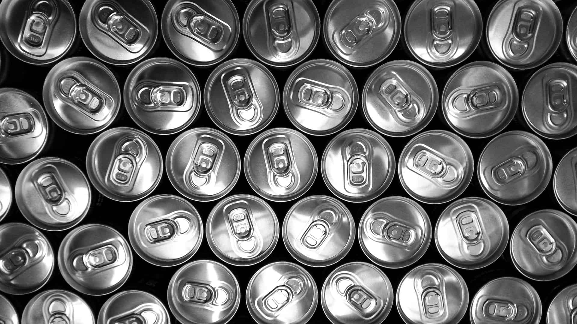 A top-down view of numerous aluminum cans arranged closely together, showing the pull-tabs and circular tops in a repetitive, orderly pattern.