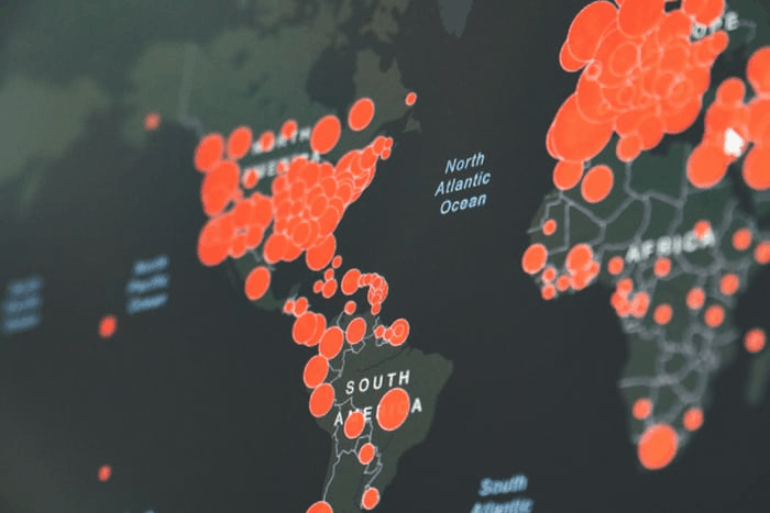 A digital world map with large red circles marking data points, showing concentrations across North and South America, Europe, and Africa, indicating widespread impact or activity in those areas.