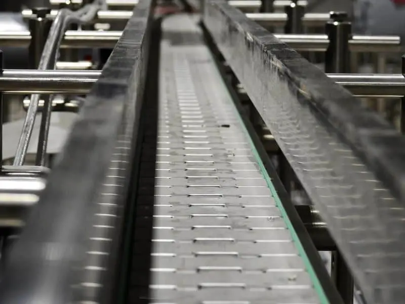 Close-up view of an empty industrial conveyor belt system with metal rails and rollers, typically used for transporting goods in a factory or manufacturing facility.