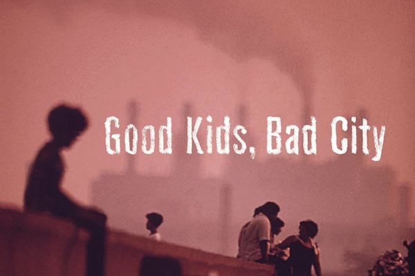 A group of silhouetted people stand and sit outdoors in front of a hazy industrial background with smokestacks. The text Good Kids, Bad City appears in bold white letters across the image.