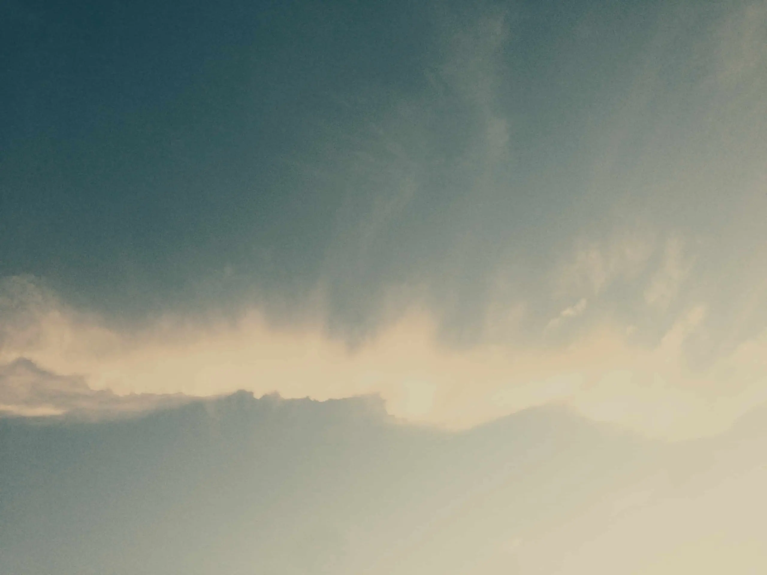 A soft, pale Heim cloud stretches horizontally across a blue sky, with sunlight creating a gentle glow along the cloud’s edge and a subtle gradient from light to dark in the sky.