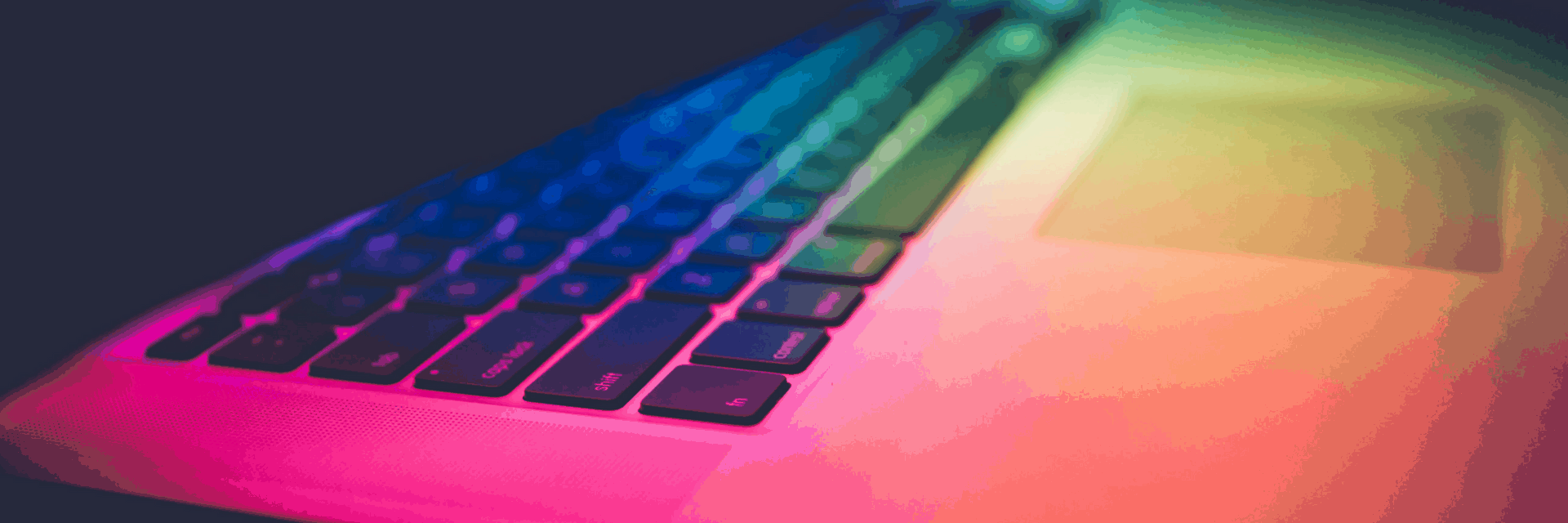 Close-up of a laptop keyboard and touchpad, illuminated by colorful rainbow lighting, creating a vibrant and modern atmosphere.