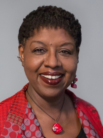 Two women smiling at the camera; the woman on the left has short curly hair and a red jacket, while her PEN Pals companion on the right has long dark hair, earrings, and a colorful top.