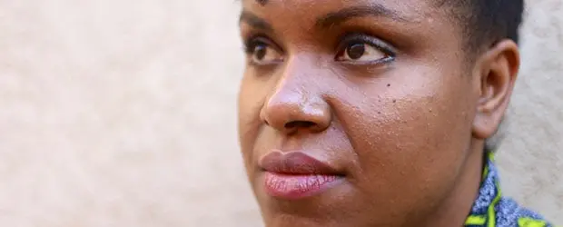 A person with short hair looks thoughtfully into the distance, their face partially turned to the side against a neutral background.