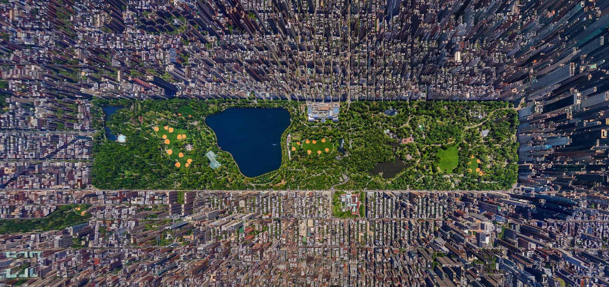 Aerial view of Central Park in New York City, surrounded by dense skyscrapers and streets, with green spaces, water bodies, and pathways visible within the park.
