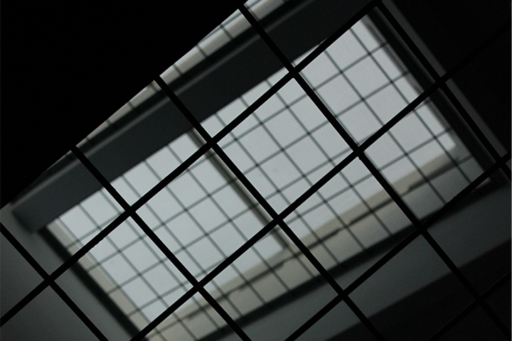 A view looking up at a large glass ceiling with a grid-like pattern, casting geometric shadows and lines. The image is taken from below, creating an abstract, architectural composition.