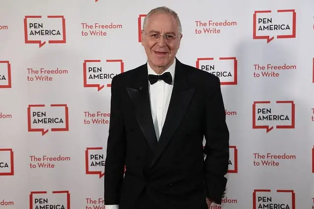 A man in a black tuxedo and bow tie smiles while standing in front of a step-and-repeat backdrop with the PEN America logo and the slogan The Freedom to Write repeated.