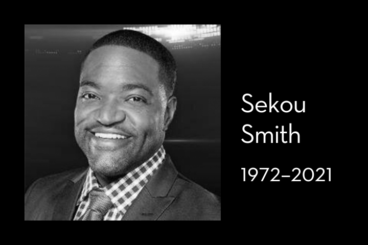 Black and white portrait of a smiling man in a suit and checkered shirt. Text beside him reads: “Sekou Smith, 1972–2021.”.