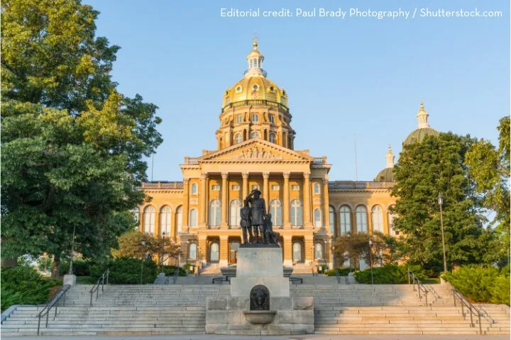 A grand building with a golden dome is seen under a blue sky, flanked by green trees. A statue stands prominently in the foreground.