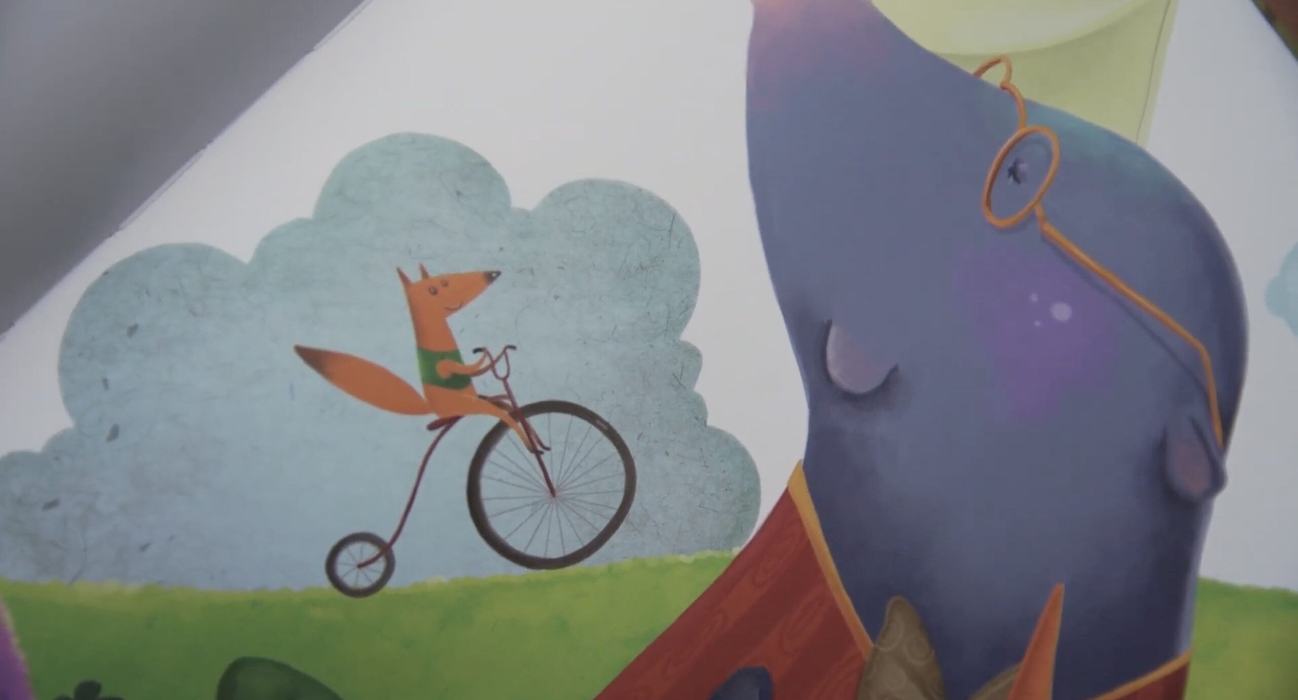 A whimsical illustration of a fox riding a penny-farthing bicycle on a grassy hill, while a large blue creature wearing glasses looks on happily. A cloud floats in the background under a pale yellow sky.