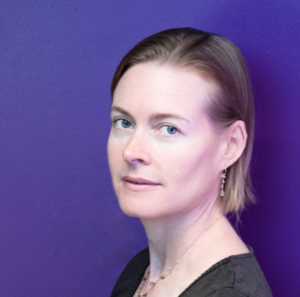 A person with short, light brown hair, wearing a dark top and earrings, poses against a vibrant purple backdrop. They have a calm expression, reminiscent of world literature speakers, and are looking directly at the camera.