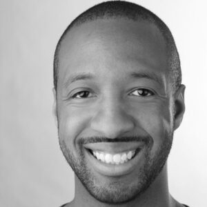 Smiling person in a black and white portrait, facing the camera with a light background.