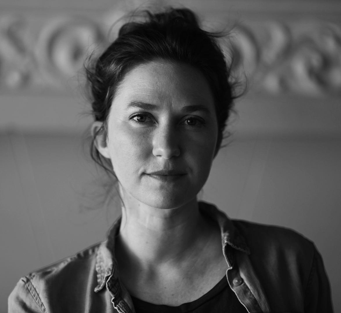 Black and white portrait of a person with medium-length hair, wearing a button-down shirt. The background has a blurred, ornate pattern. The lighting casts soft shadows, creating a contemplative and serene expression on their face.