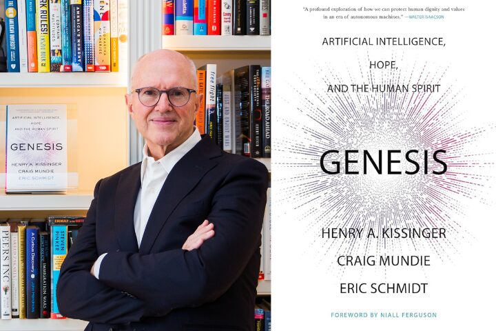 A bald man wearing glasses and a dark suit stands with arms crossed in front of a bookshelf. Next to him is a book cover titled Genesis by Henry A. Kissinger, Craig Mundie, and Eric Schmidt, featuring a starburst design.