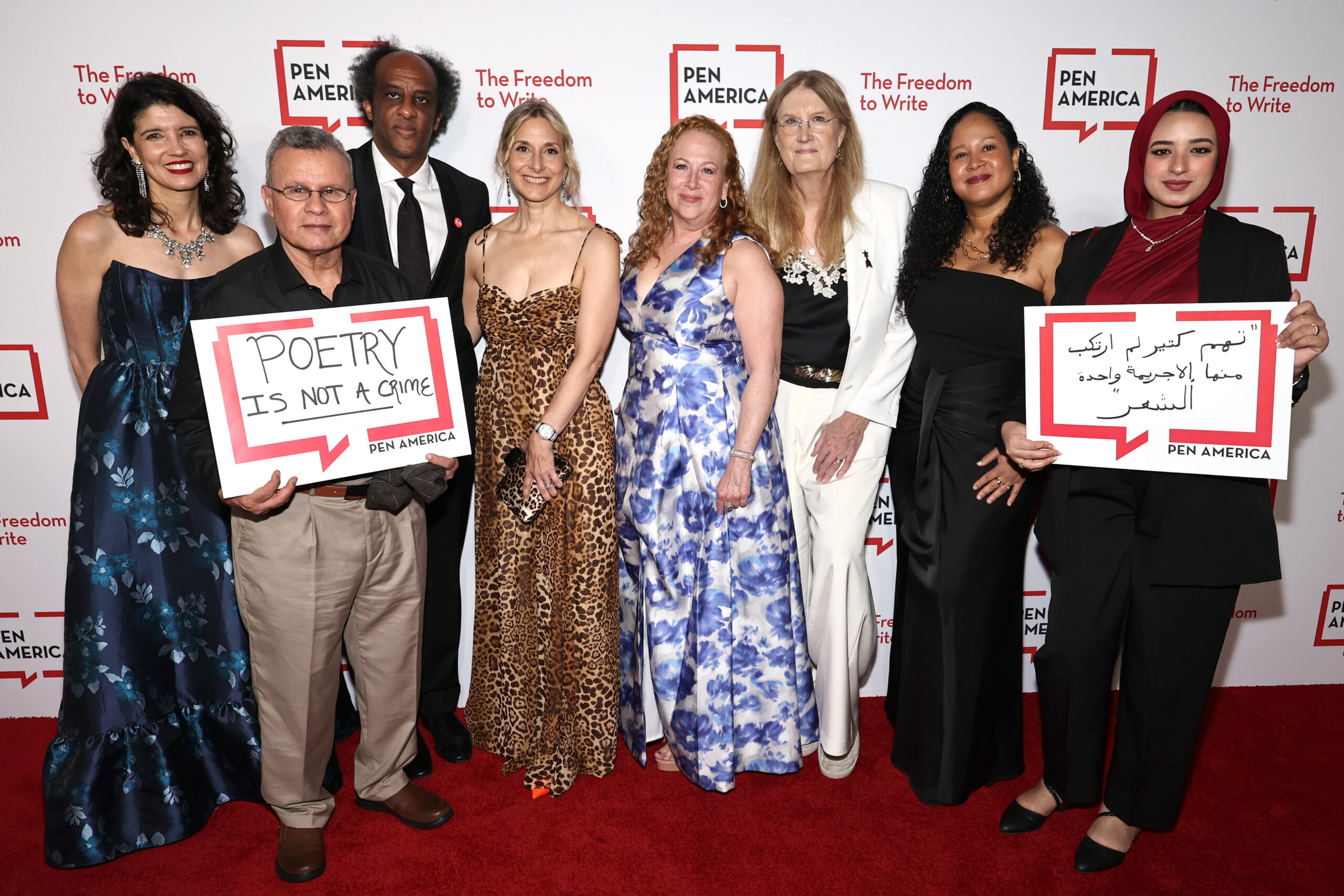 Eight people stand on a red carpet at a PEN America event. Two hold signs reading “POETRY IS NOT A CRIME” and text in Arabic. The backdrop features the PEN America logo and the phrase The Freedom to Write.