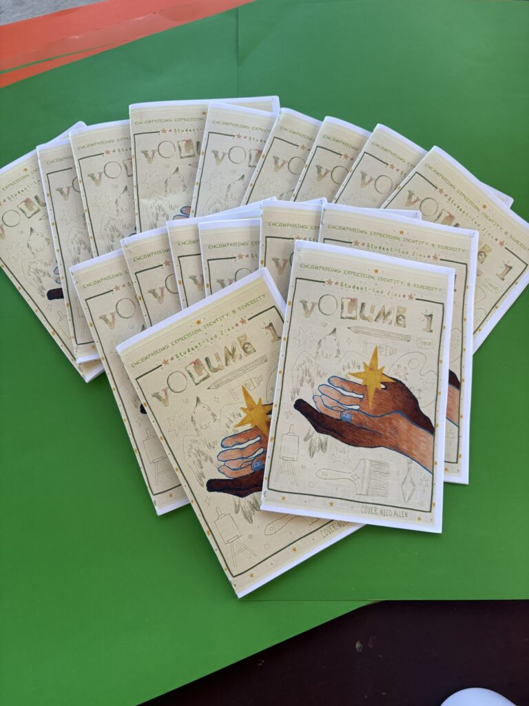 A stack of booklets titled Volume 1 with illustrated covers showing two hands reaching toward a gold star, arranged on a green and red background.