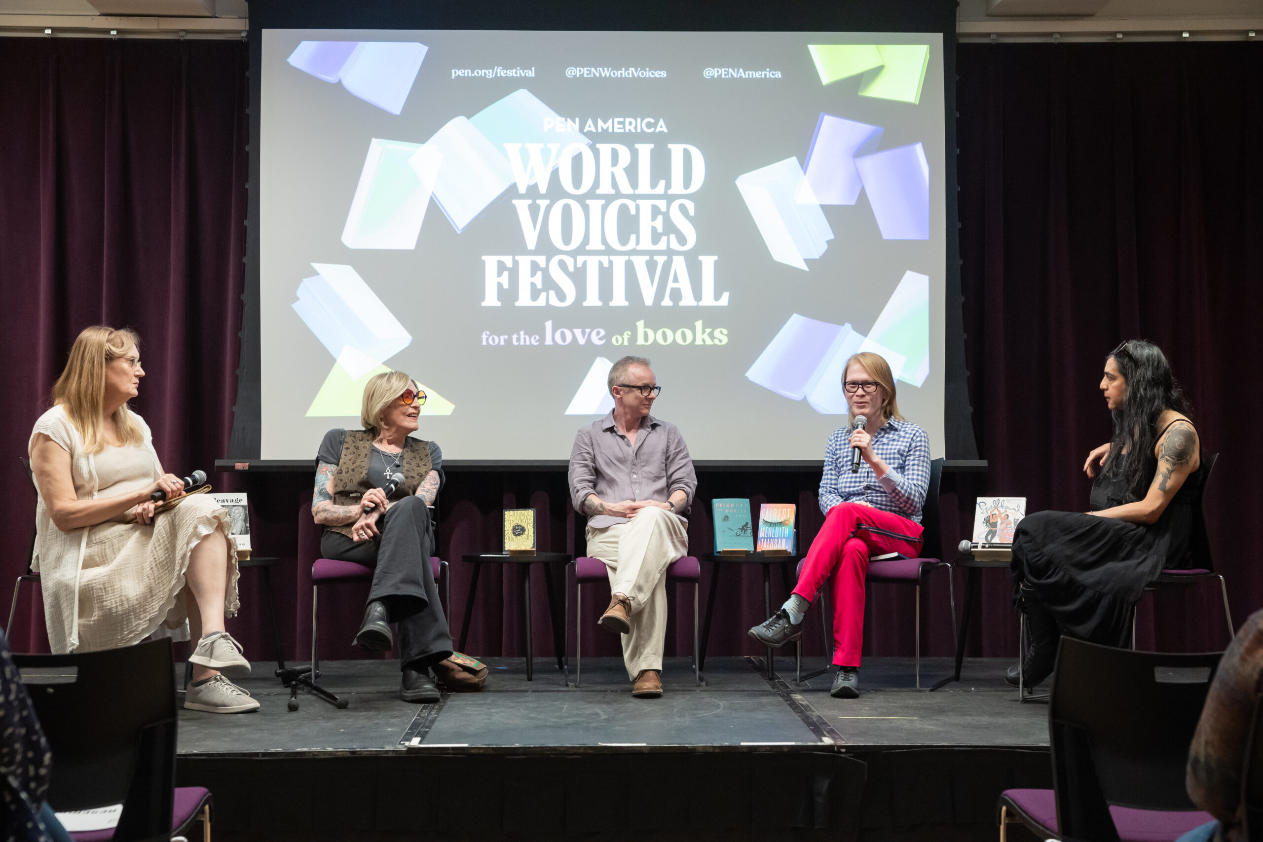 Five speakers sit on stage in front of a screen reading “PEN America World Voices Festival for the love of books,” engaging in a panel discussion. There are books displayed on the table in front of them.