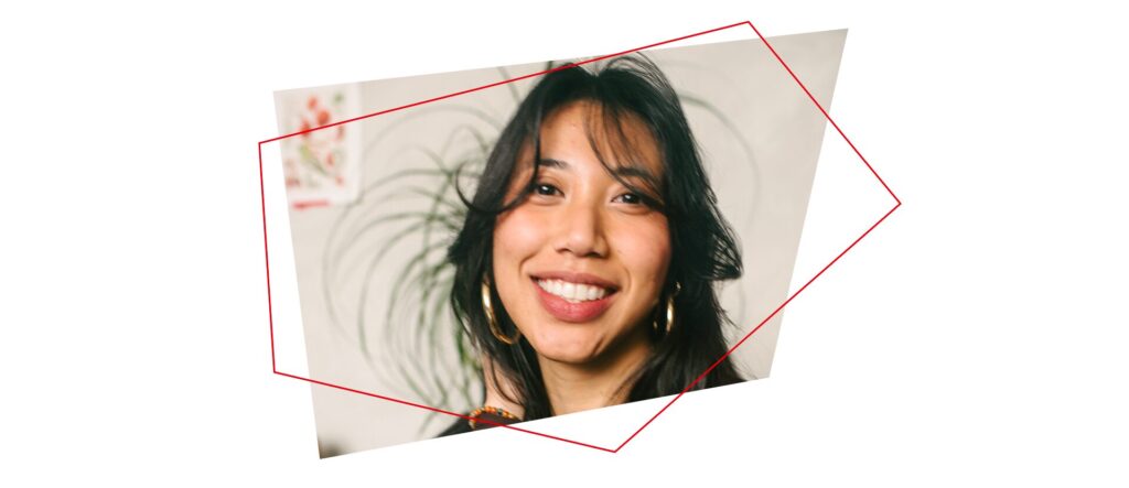 A woman with long dark hair and hoop earrings smiles at the camera. A plant with long leaves is in the background, and a red geometric outline frames the image.