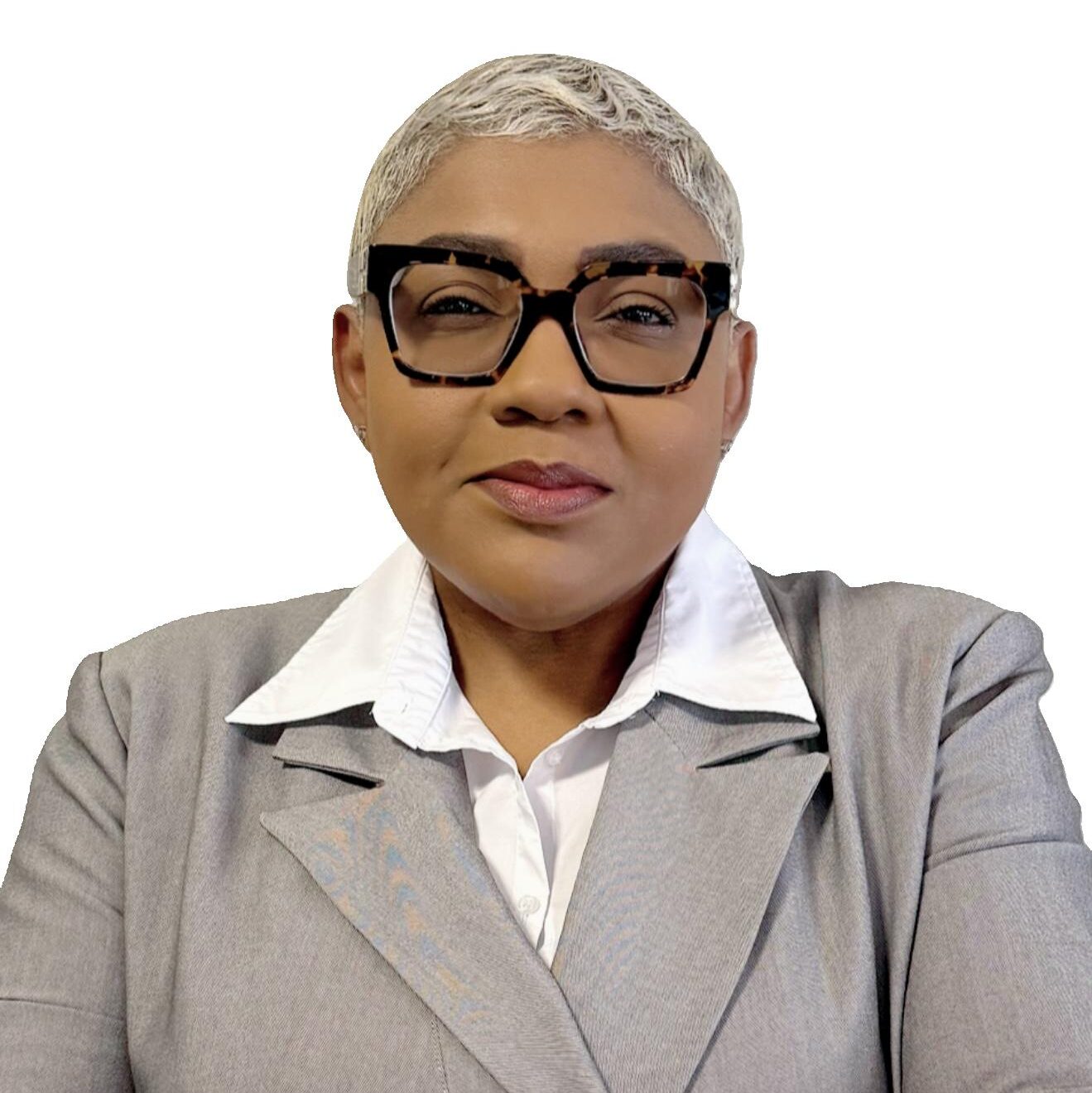 A person with short, gray hair and large, dark-rimmed glasses wears a light gray suit jacket over a white collared shirt, posing against a plain white background.