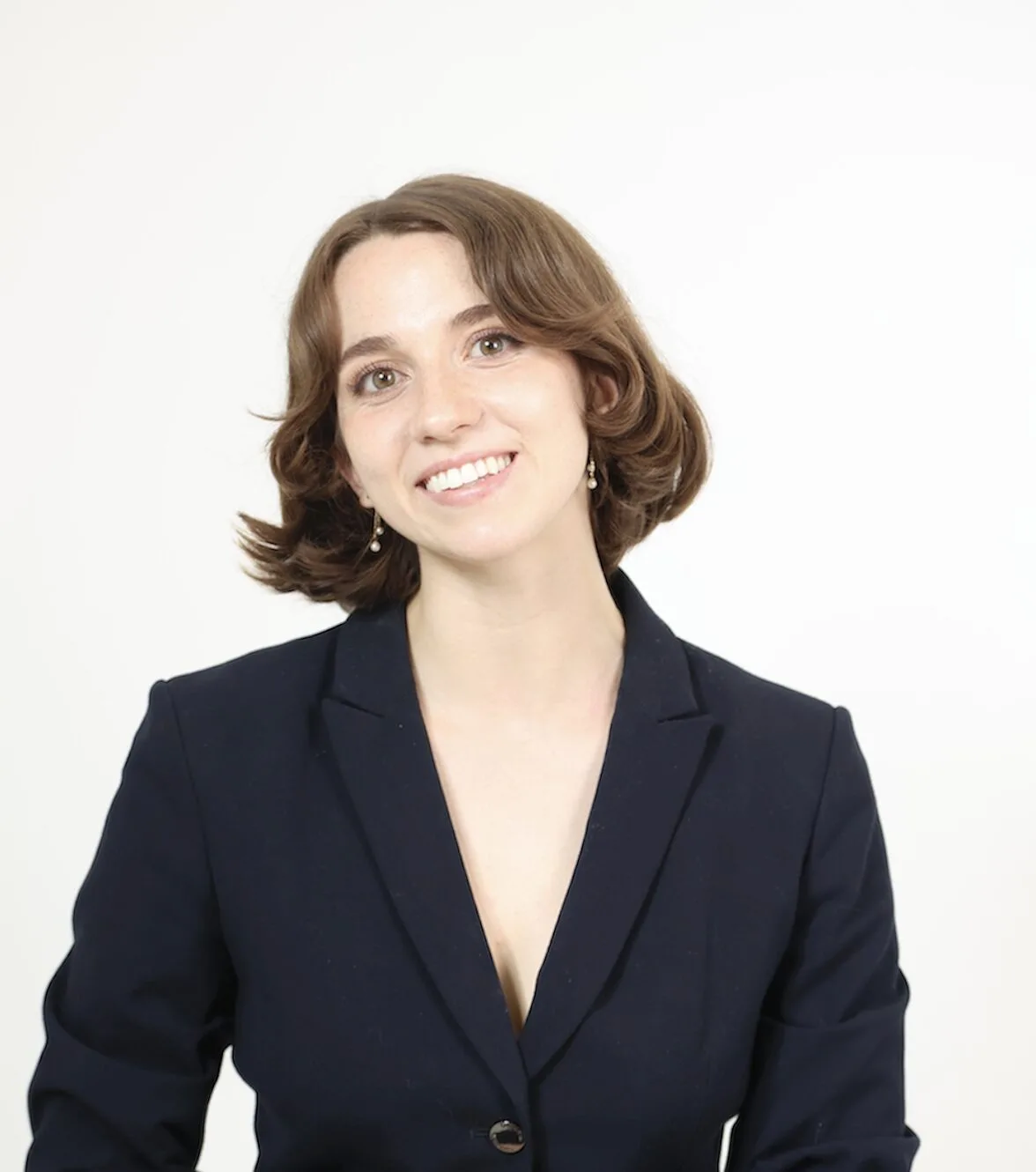 A woman with short brown hair, wearing a dark blazer, smiles at the camera against a plain white background.