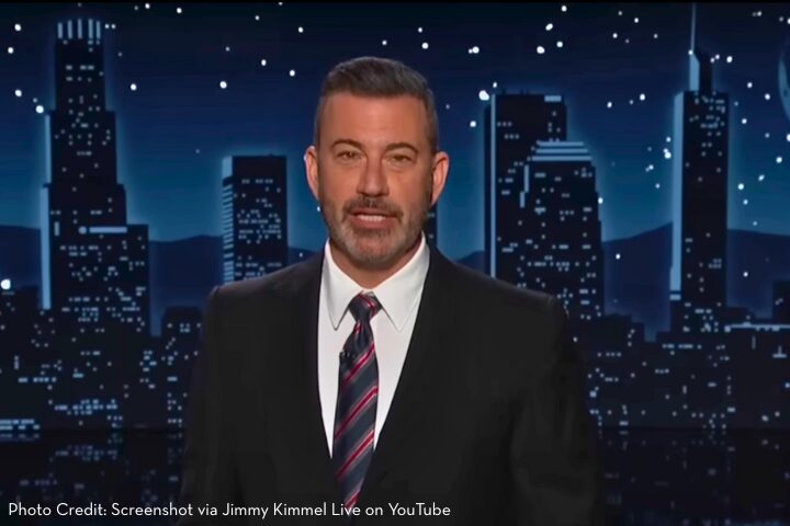 A man in a dark suit and striped tie stands on a stage with a city skyline backdrop and starry night sky. Text at the bottom credits Jimmy Kimmel Live on YouTube.