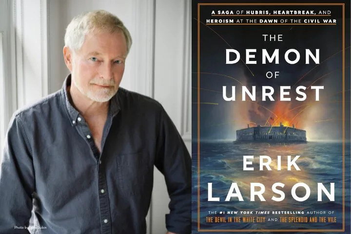 Author Erik Larson stands beside the cover of his book The Demon of Unrest, which features an image of a burning fort at sea under a dark sky, with bold white and orange title text.