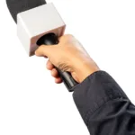 A person wearing a black long-sleeve shirt holds a handheld microphone with a square windscreen, extending it forward against a white background.