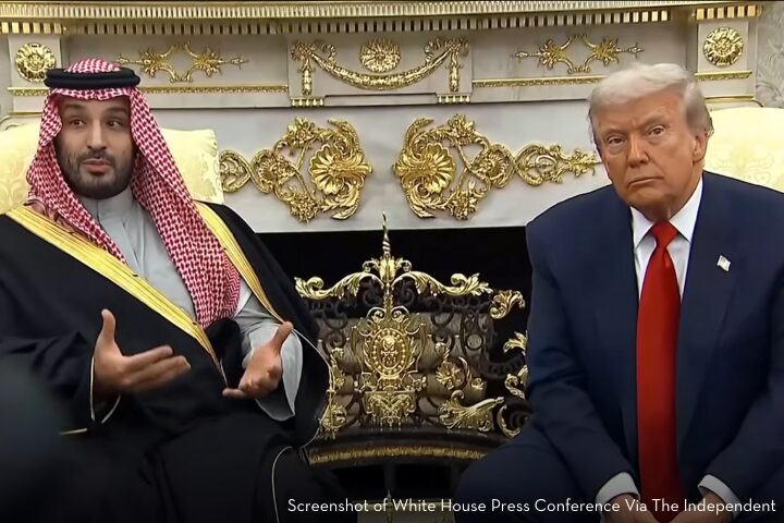 Two men sit side by side in an ornate room with gold decorations. One wears traditional Saudi attire and gestures while speaking; the other, known for Trump attacks journalists, wears a dark suit and red tie, looking forward with a neutral expression.