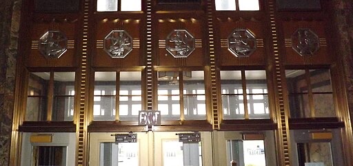 Art Deco-style interior doors with decorative metallic reliefs above, featuring geometric patterns and figures. The doors have glass panels and an illuminated EXIT sign above the center doorway.