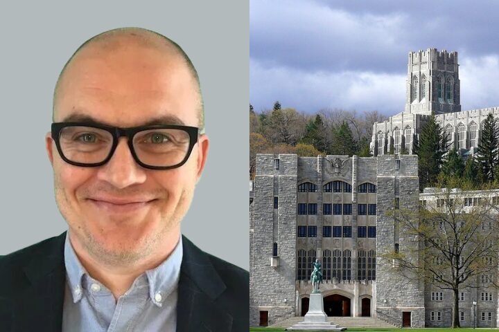 A man with glasses and a suit smiles at the camera on the left; on the right is a large stone building with a statue and a tall tower, surrounded by trees.